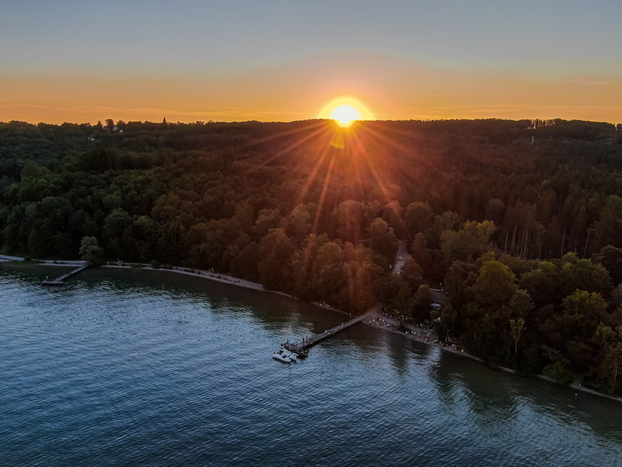 Steg von oben mit Sonne hinter den Bäumen am Starnberger See