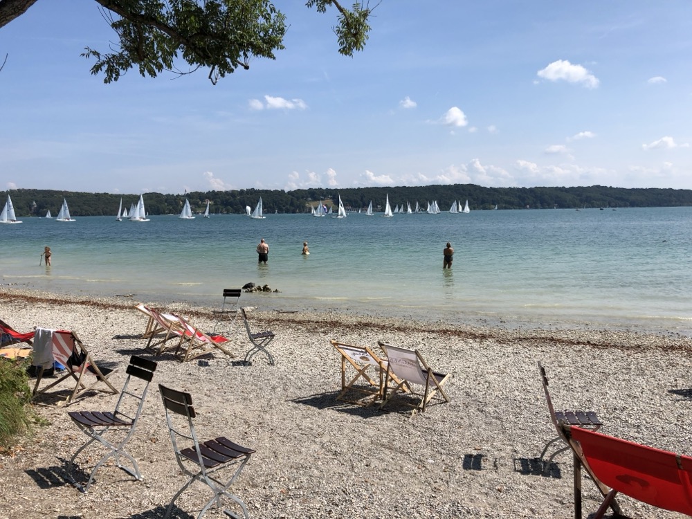 Liegestühle am Kiesstrand mit Segelbooten auf dem See