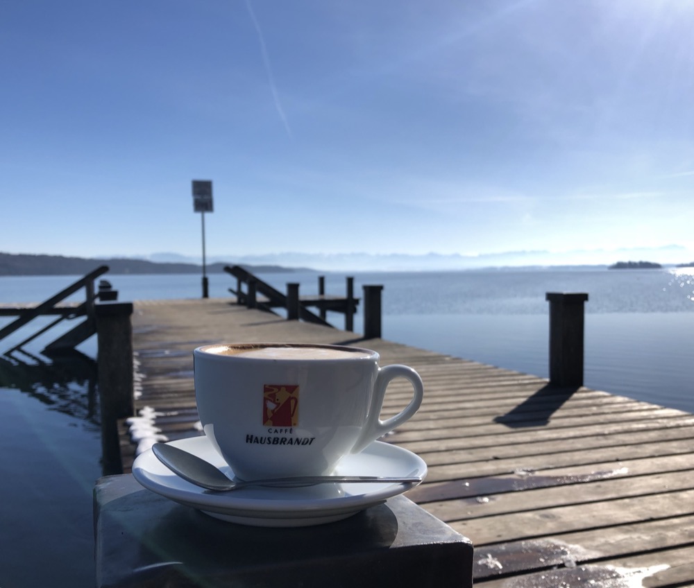 Kaffeetasse auf dem Steg mit Blick auf den ruhigen Wintersee